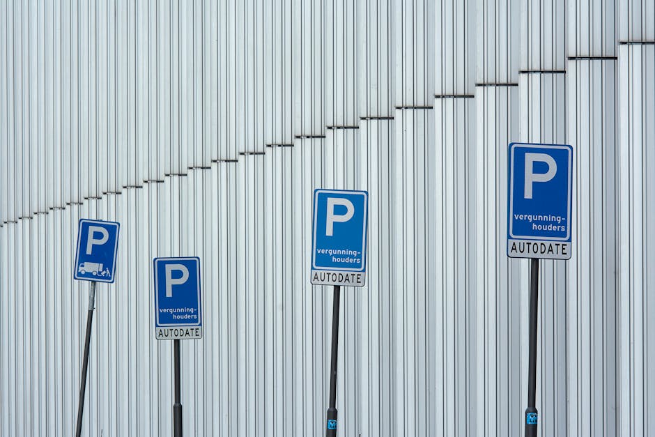 Four blue parking permit signs mounted on slim metal posts in front of a modern exterior wall composed of vertical silver metal panels. The signs display a prominent white 'P' for parking, with additi